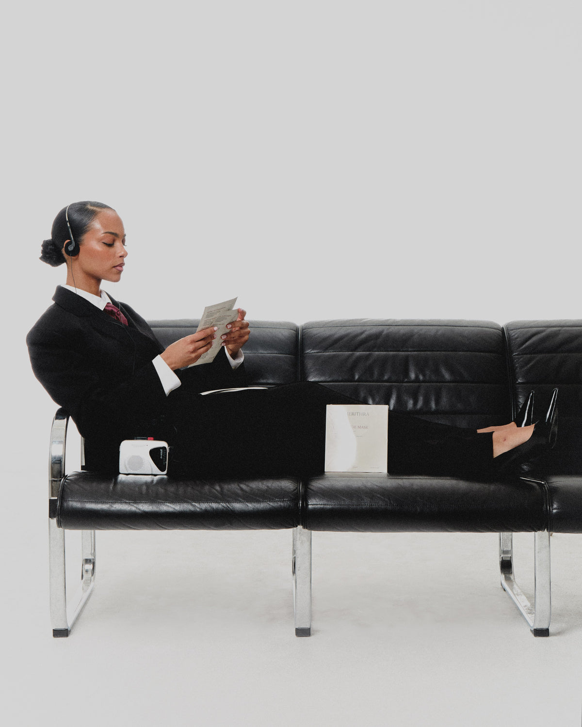 Model in a black suit on a leather bench with The Peptide Mask